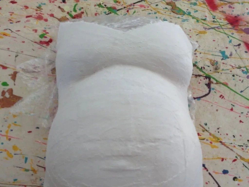 A white pillow shaped like a pregnant woman 's belly.