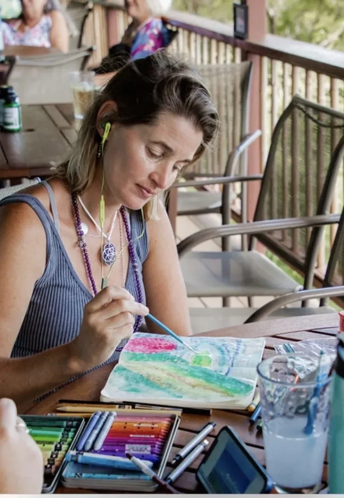 A woman painting with watercolors on top of a table.