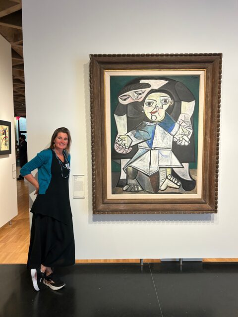 A woman stands beside a framed Picasso painting in a gallery.